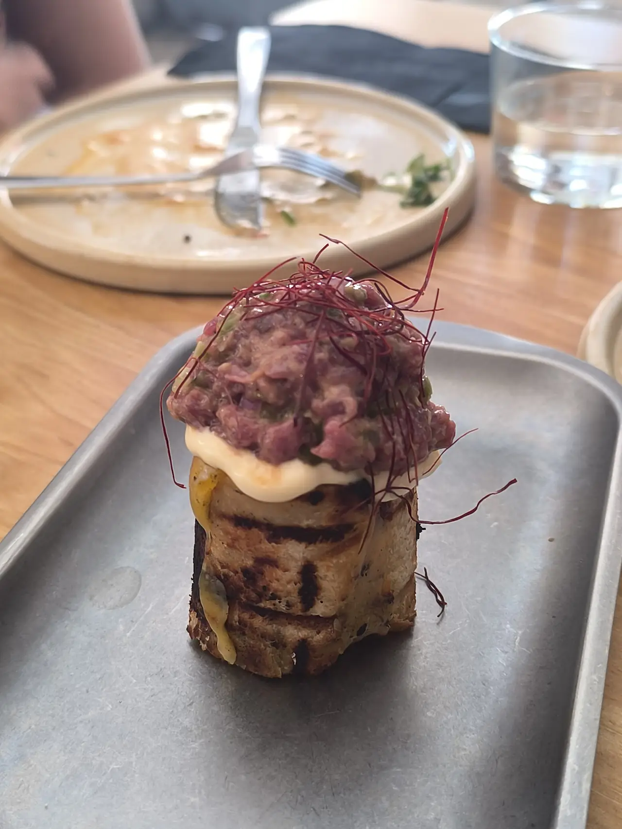 Toasted bread topped with cheese, beef tartare and beetroot sprouts, plated on a metal tray