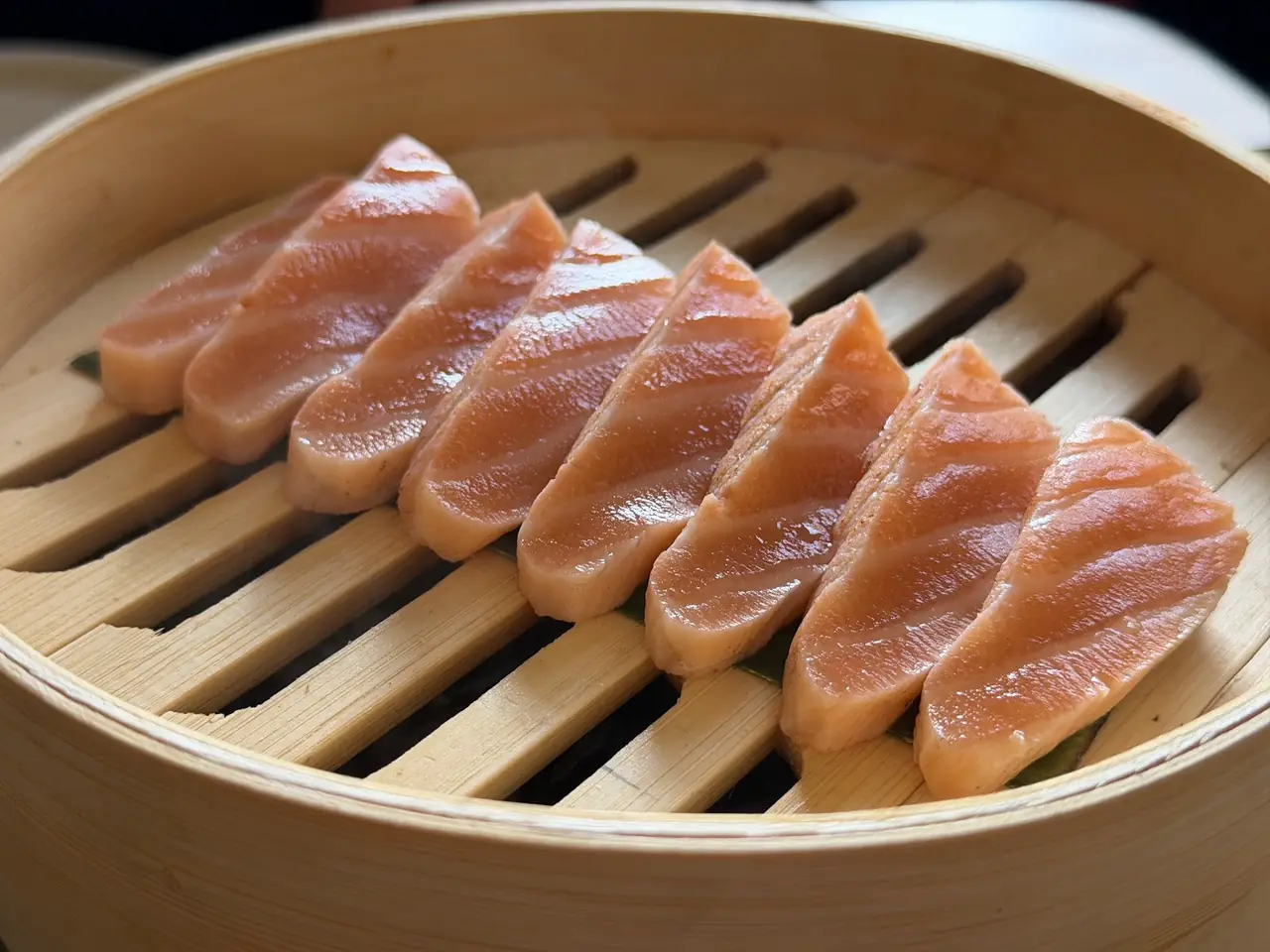 Sliced grilled fish fillets fanned out in a bamboo steamer basket