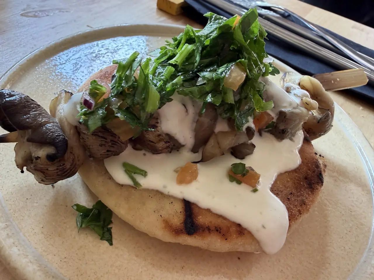 Grilled flatbread topped with cream sauce, herbs and a grilled mushroom skewer