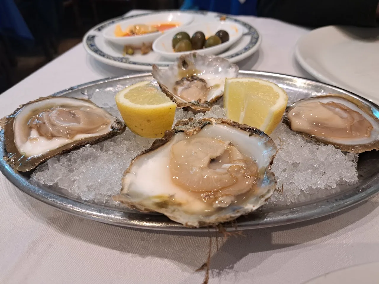 A silver platter of oysters on ice with lemon wedges