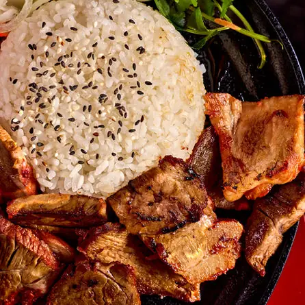 Close-up of a mound of sesame-topped white rice beside grilled marinated pork pieces