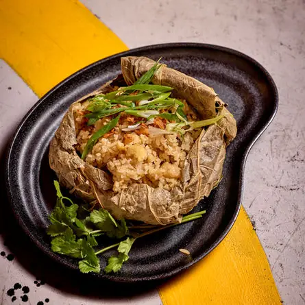 Steamed sticky rice wrapped in a lotus leaf, topped with spring onion, on a black plate