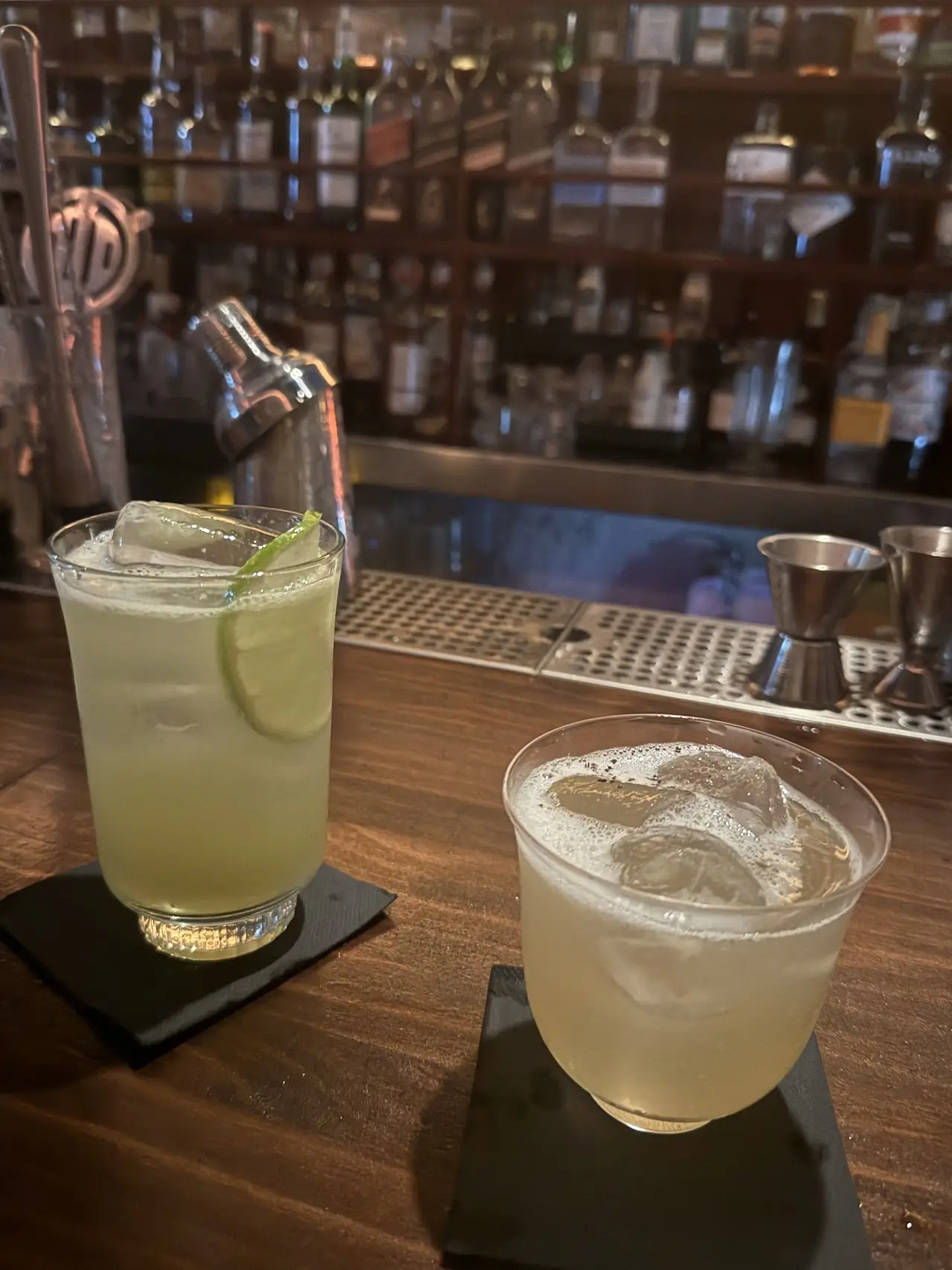 Two pale cocktails on a bar counter, one garnished with a lime wheel