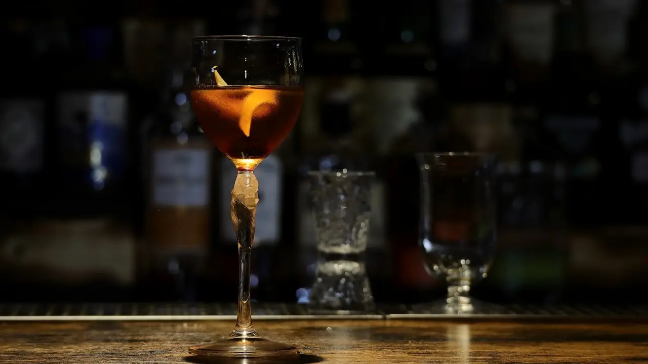 An amber cocktail with a citrus peel in a stemmed glass on the bar