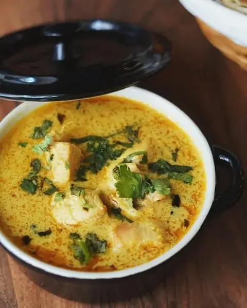Creamy yellow chicken curry garnished with coriander in a black cocotte with its lid ajar
