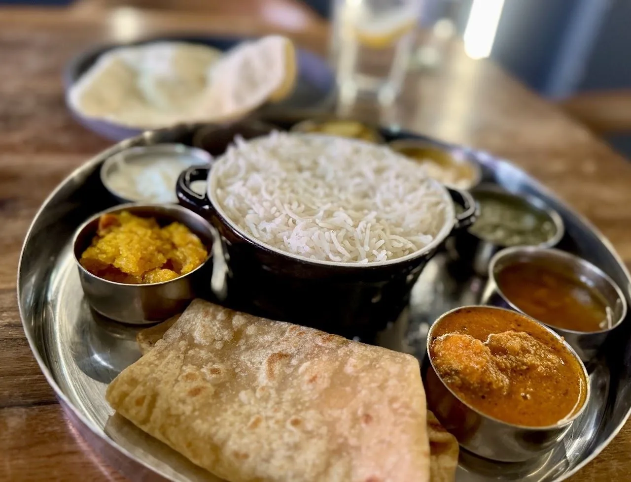 A steel thali tray with rice, flatbread, a bowl of curry and several small dishes