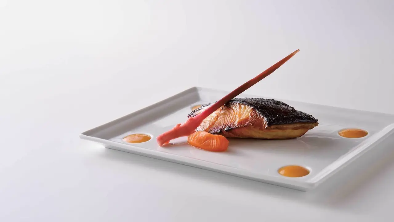 Black cod glazed with sweet miso and topped with a pickled ginger shard, served on a white rectangular plate with citrus miso dots, at Nobu