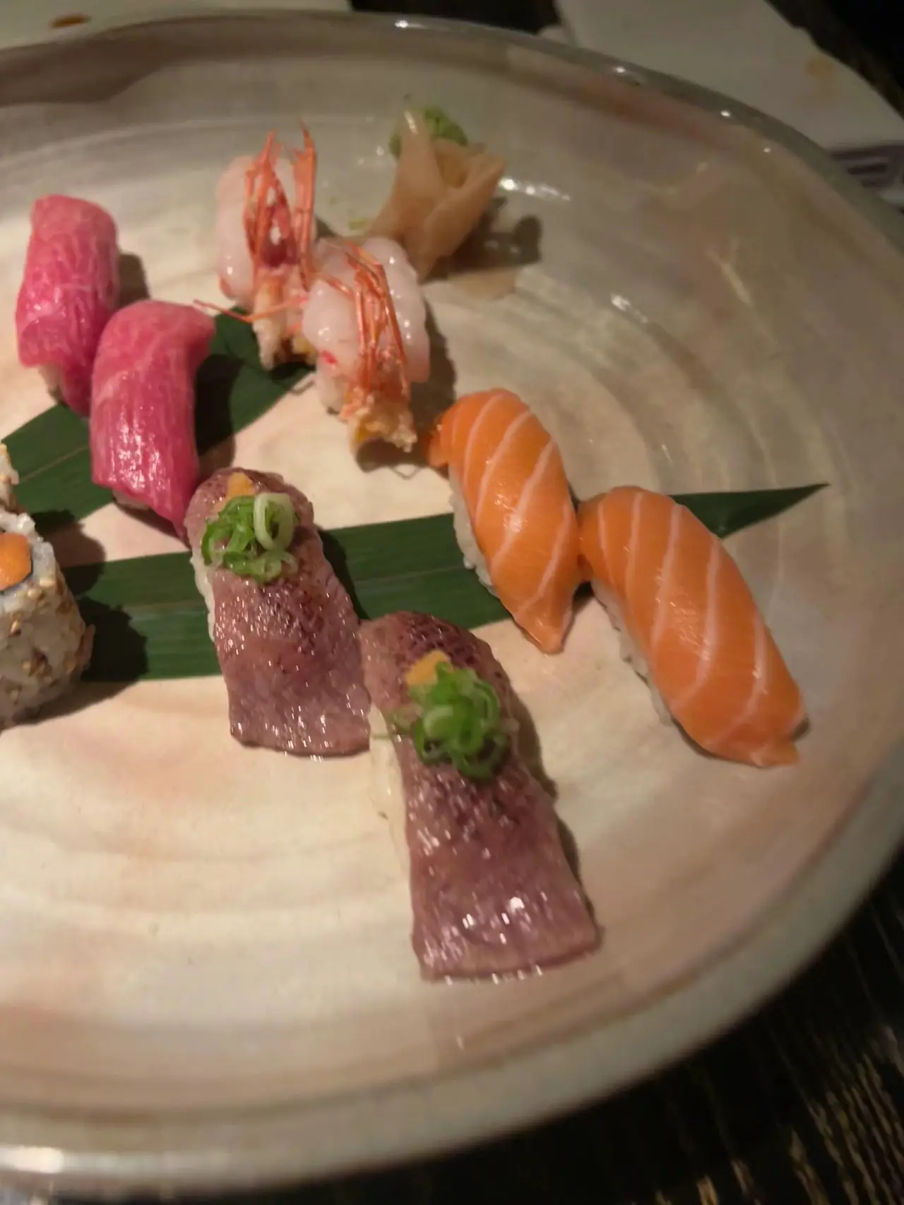 An assortment of nigiri sushi pieces, including tuna, shrimp, and salmon, arranged on a round plate.