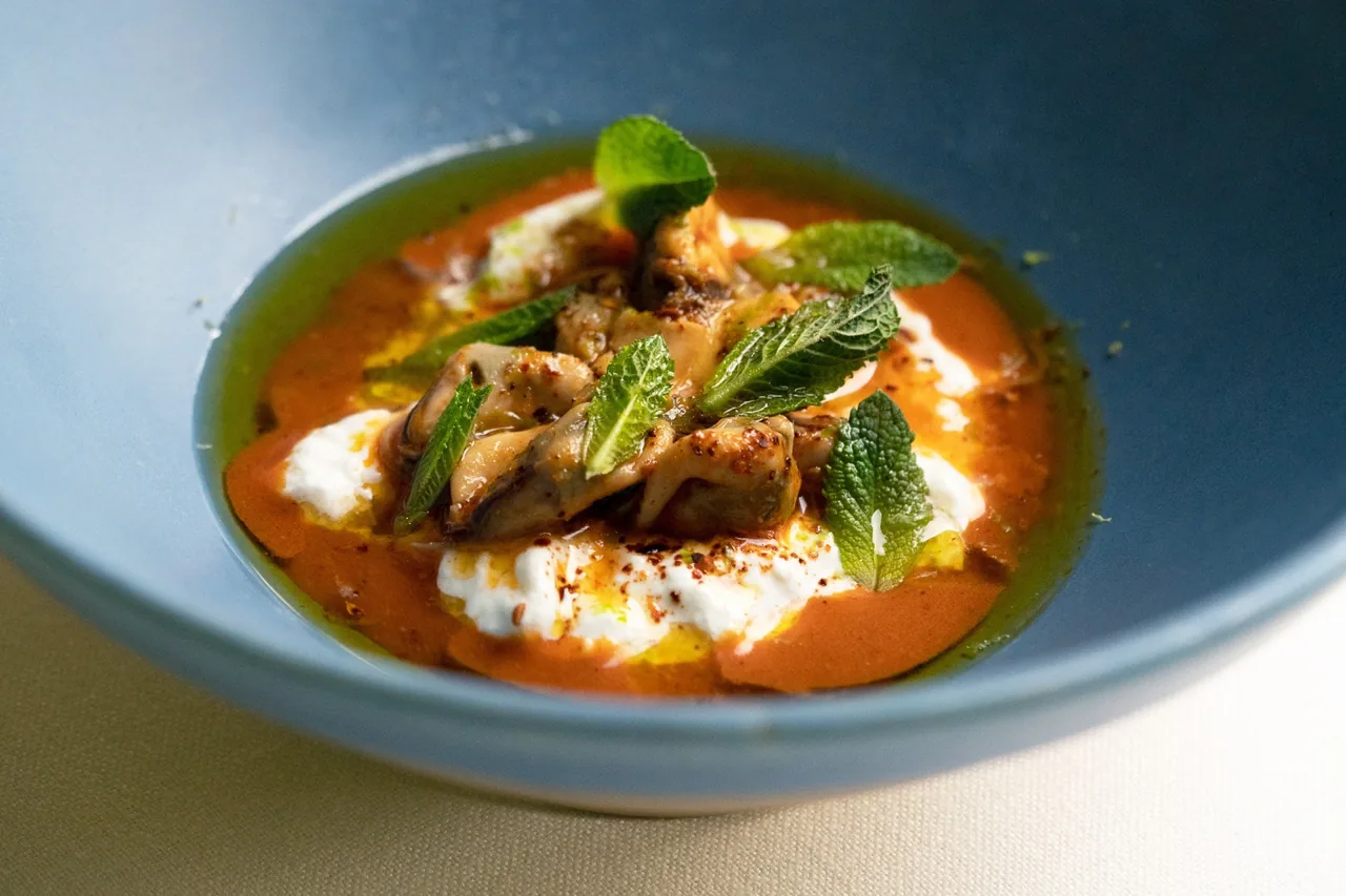 A blue bowl of a dish in orange sauce with cream and basil leaves