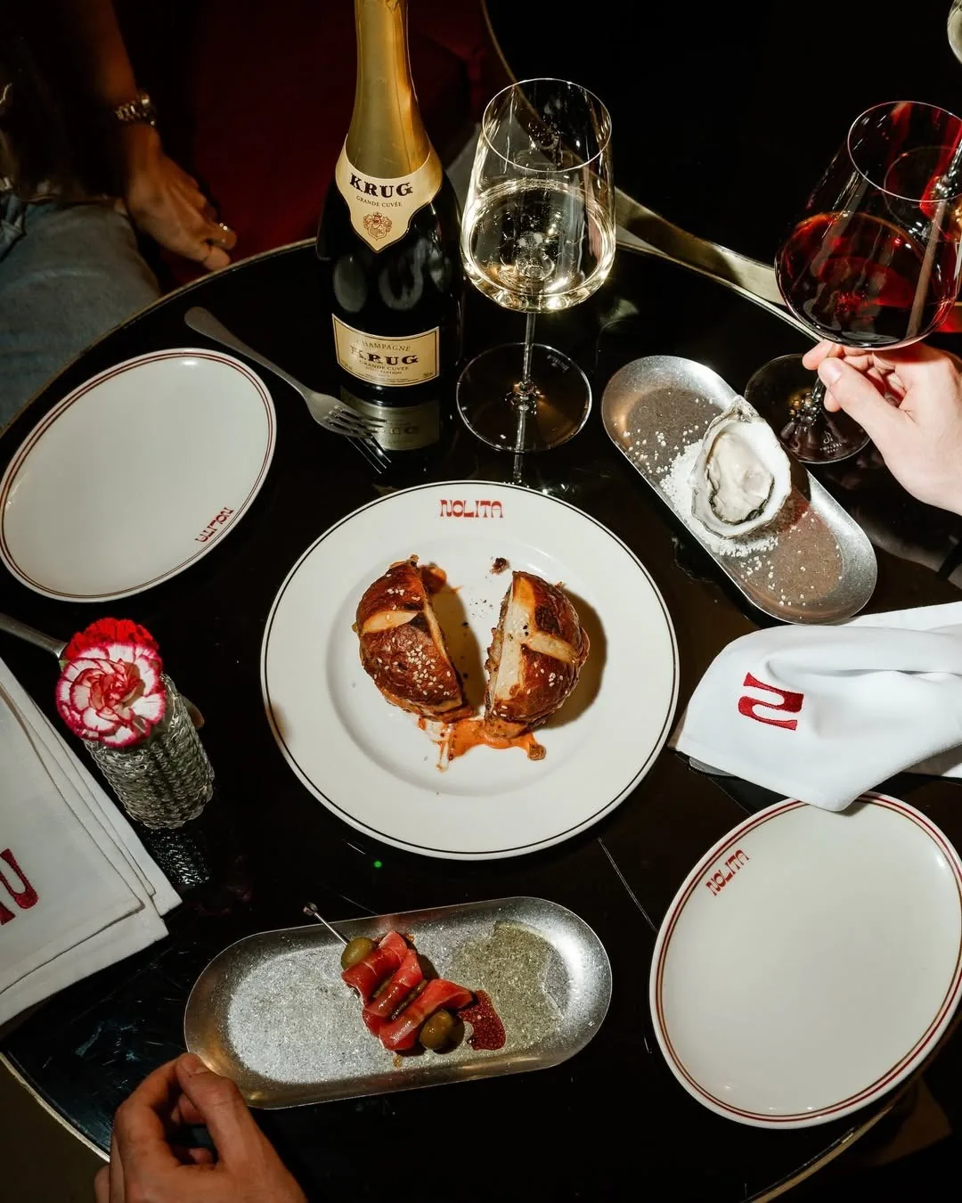 An overhead view of a dark table with a plated burger, a small tray of meat and glasses