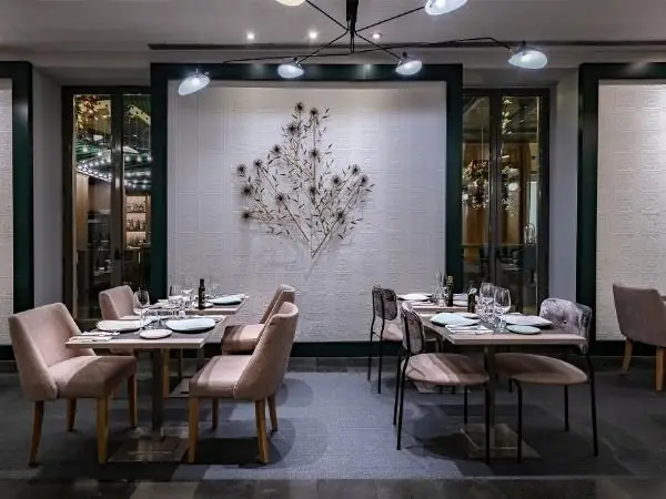 Refined dining room with pink upholstered chairs, set tables and a metal thistle sculpture on a white textured wall