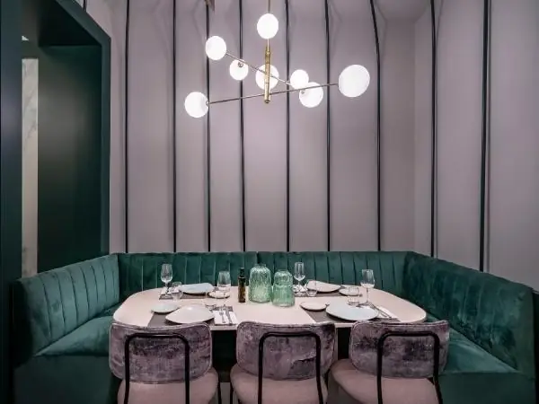 Corner booth with a green velvet banquette, a set table and a brass-and-globe chandelier against a grey panelled wall