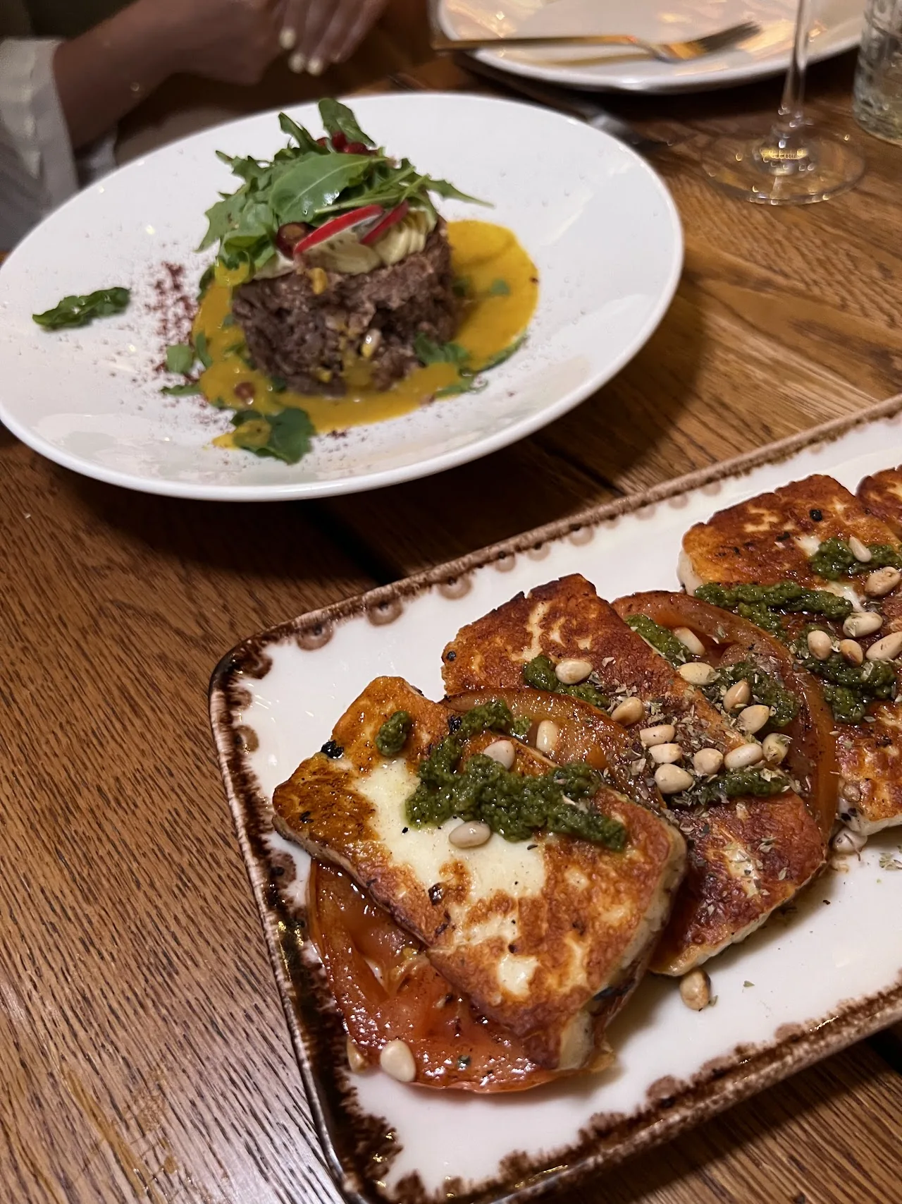 A plated meat dish with greens next to grilled bread with toppings