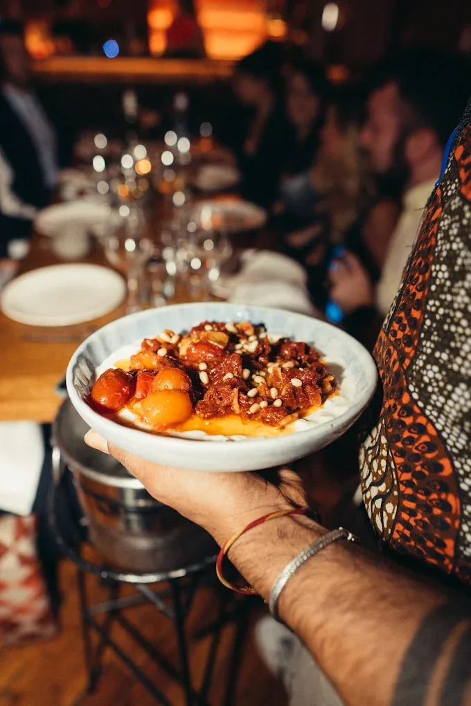 A hand holding out a plate of food with citrus garnish