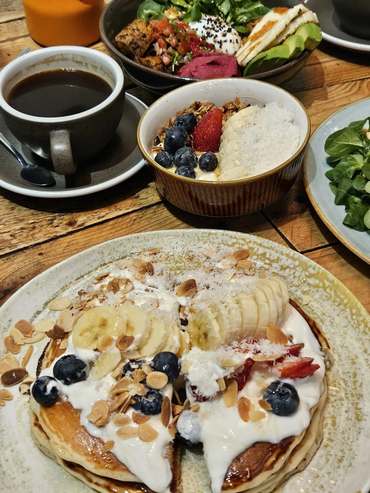 Overhead view of pancakes with banana and berries beside granola bowls