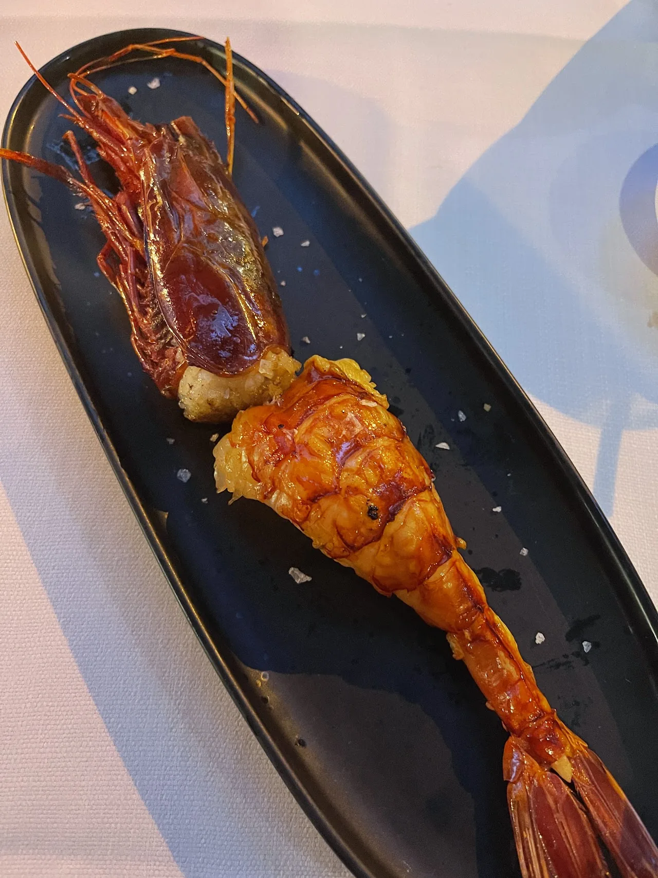 A whole grilled prawn served on a dark oval plate