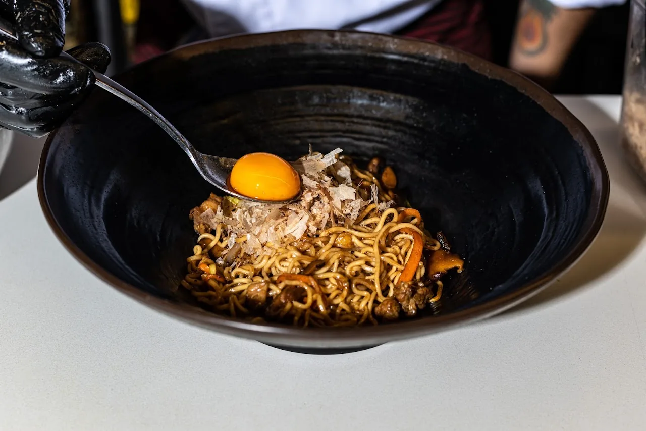 A noodle dish topped with a raw egg yolk in a dark bowl
