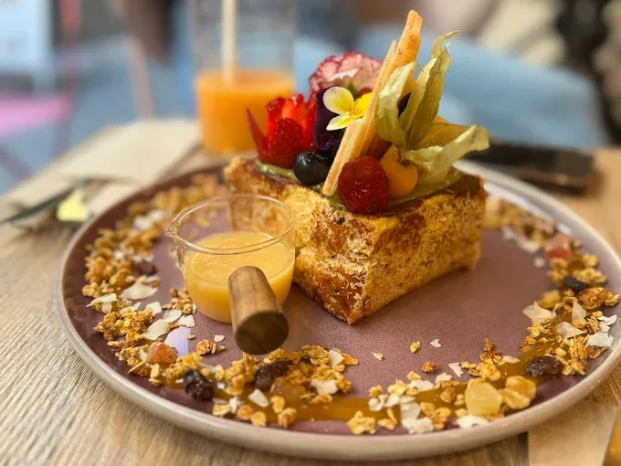 French toast plated with a fruit skewer, granola and edible flowers