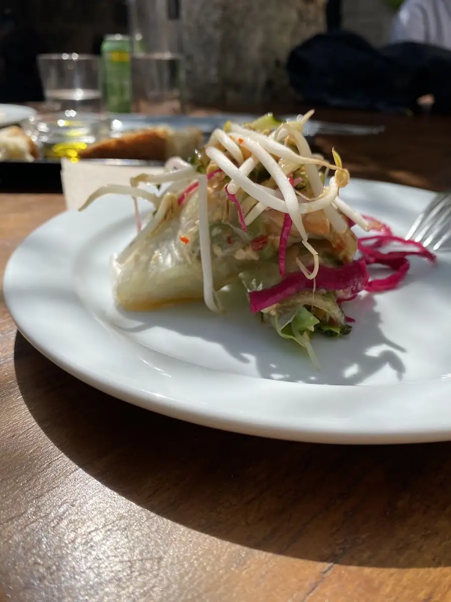 A NU dish: a dumpling topped with pickled vegetables and shoots on a white plate