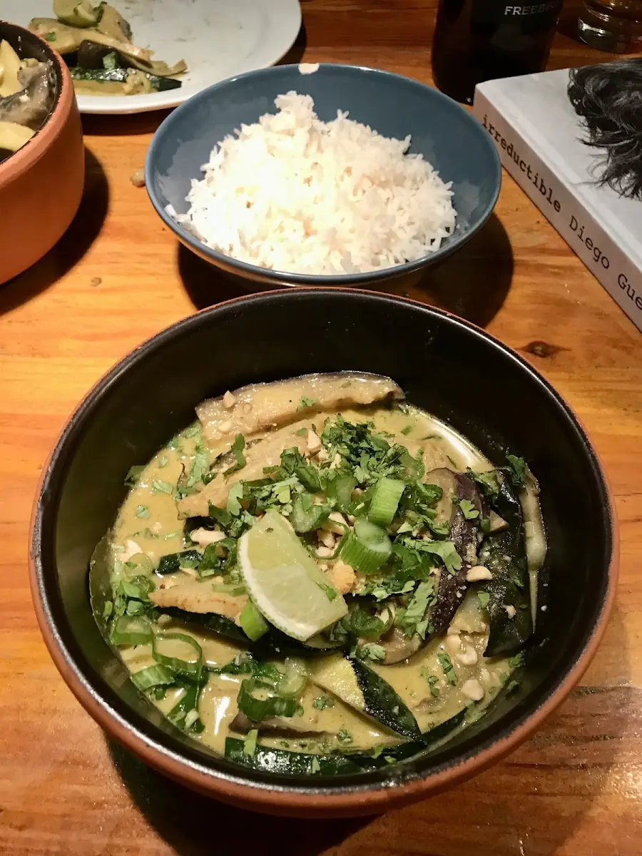 A NU dish: a green curry with vegetables and lime in a dark bowl, with rice alongside