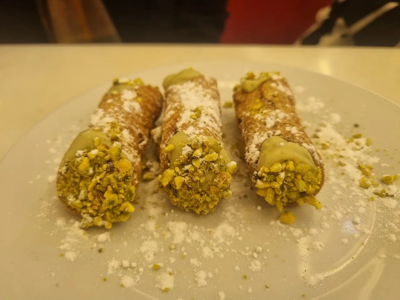 Three cannoli dusted with powdered sugar and crushed pistachio