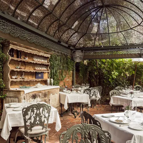 Terrace dining area with an antique wooden shelving unit, set tables, and greenery climbing the walls