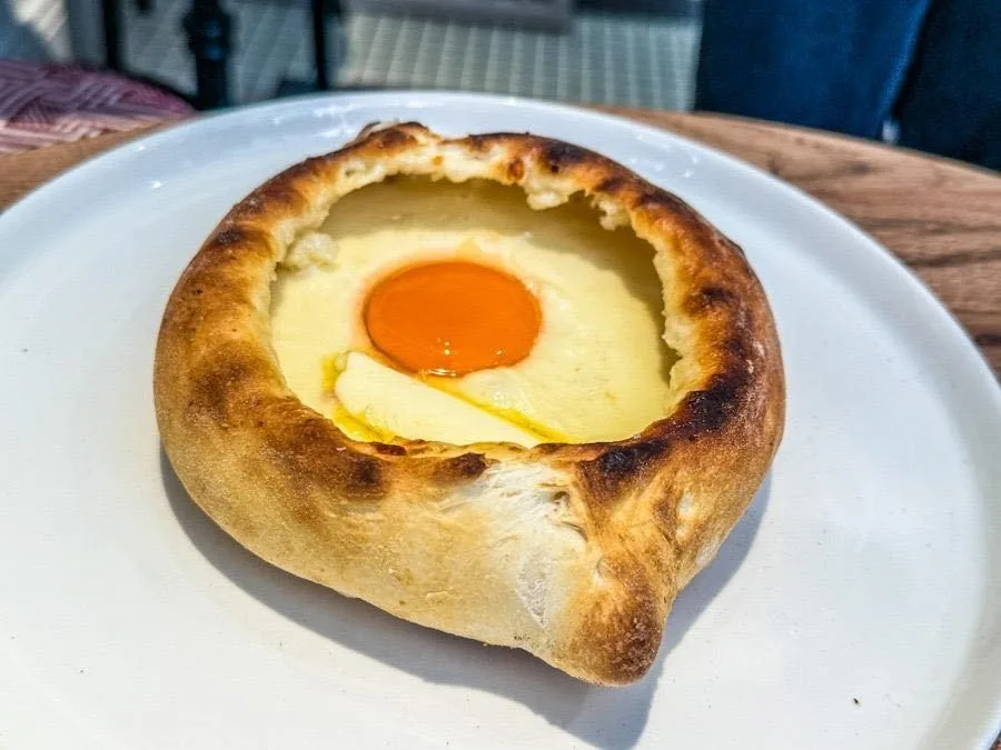 A baked bread boat filled with cheese and an egg yolk on a white plate