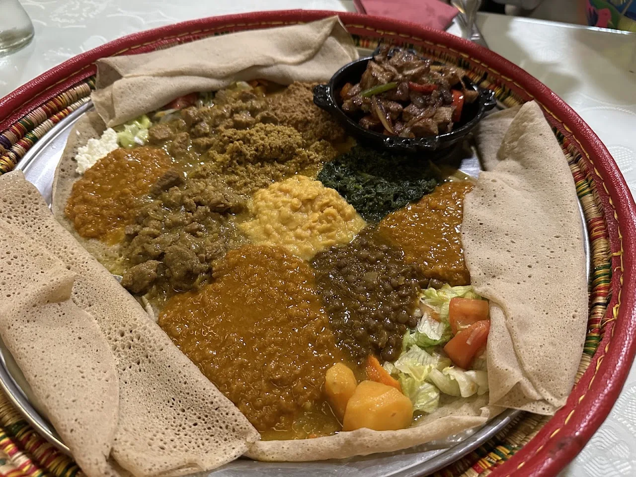 A large shared platter of injera flatbread with assorted stews and vegetables