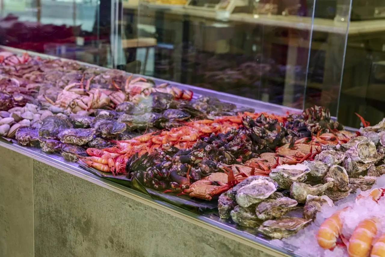 Refrigerated seafood display case piled with oysters, prawns, crabs, clams and goose barnacles on ice