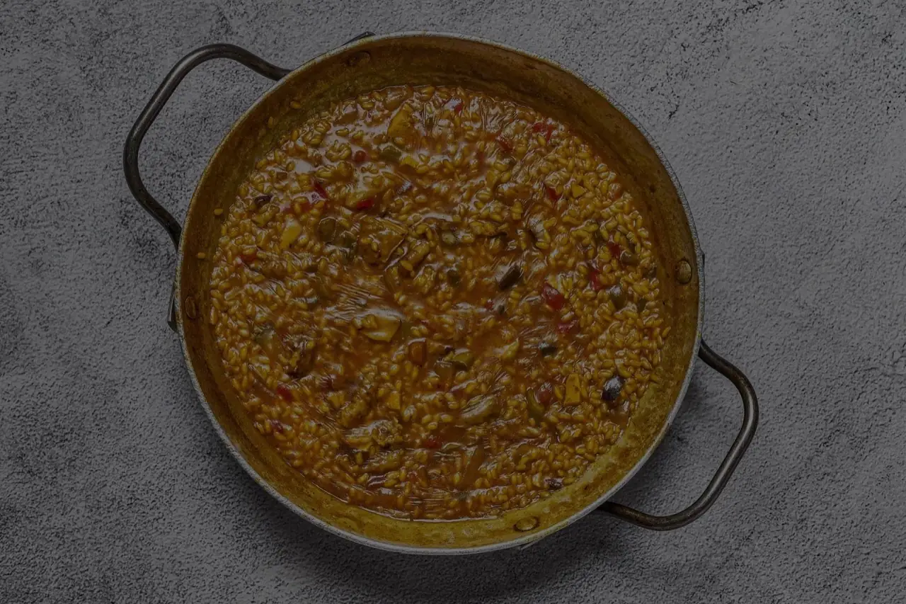 Soupy Spanish rice (arroz meloso) with vegetables in a two-handled metal paella pan on a grey surface