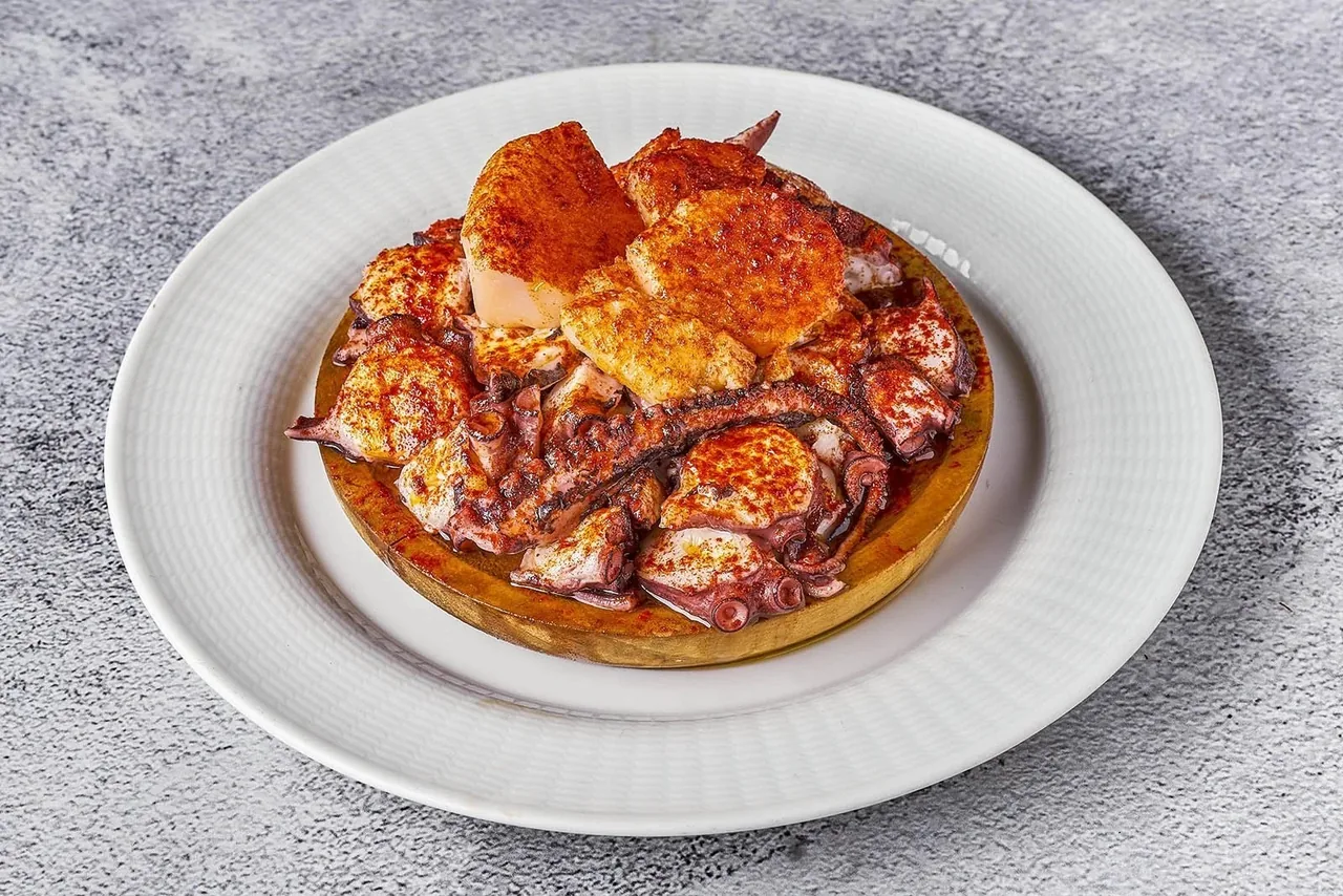 Pieces of octopus in orange sauce stacked on a white plate