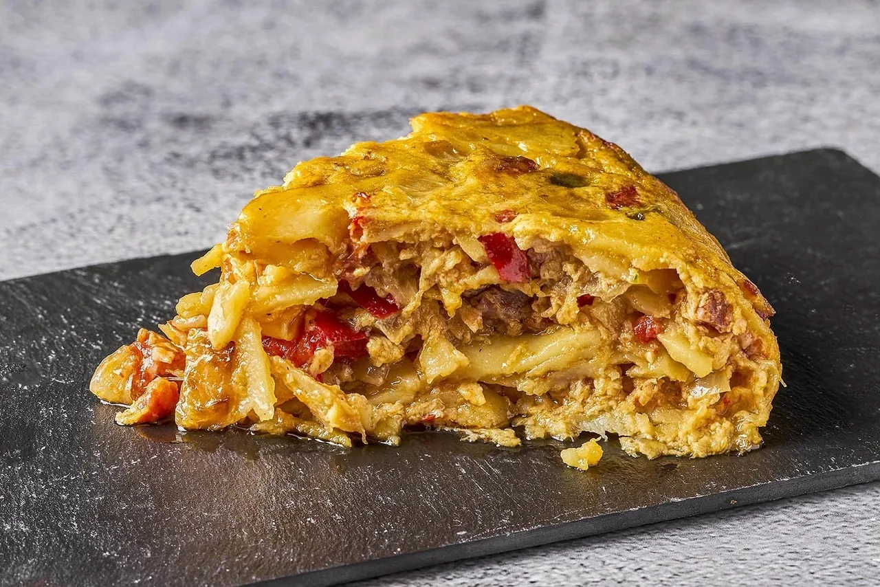 A thick slice of potato omelette on a dark slate board