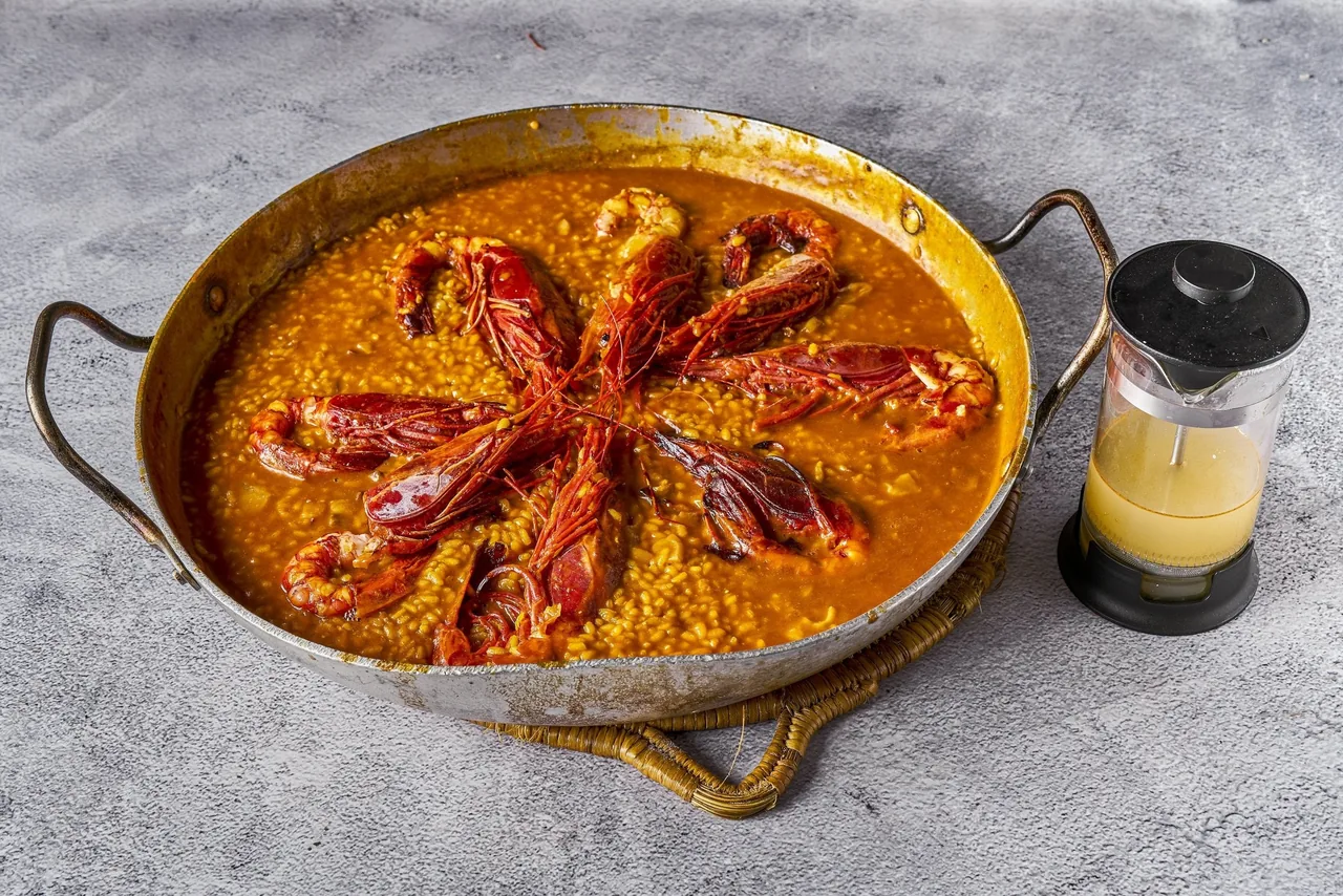 A round pan of orange rice topped with two red prawns