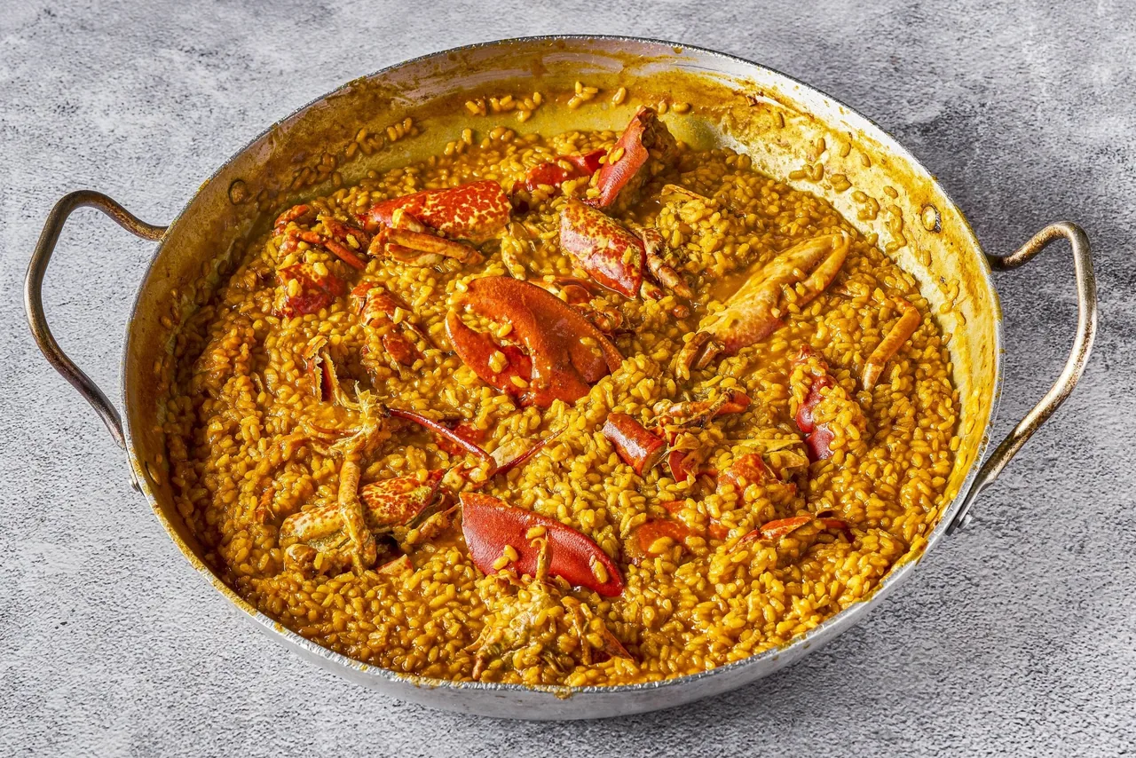 A round pan of orange rice with crab on a grey surface