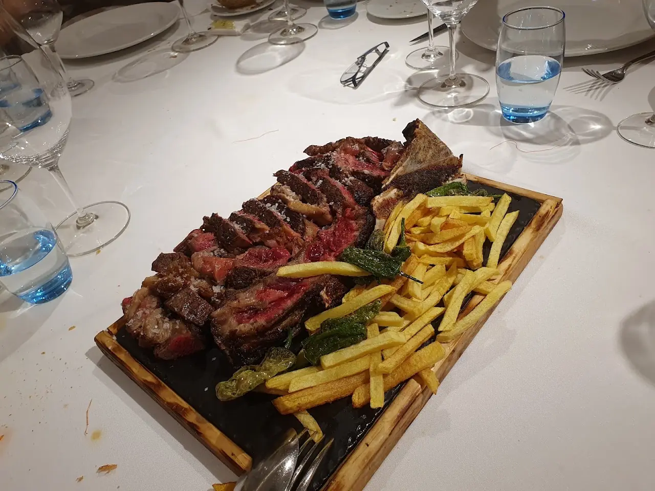 Sliced grilled steak on a wooden board with french fries and fried peppers.