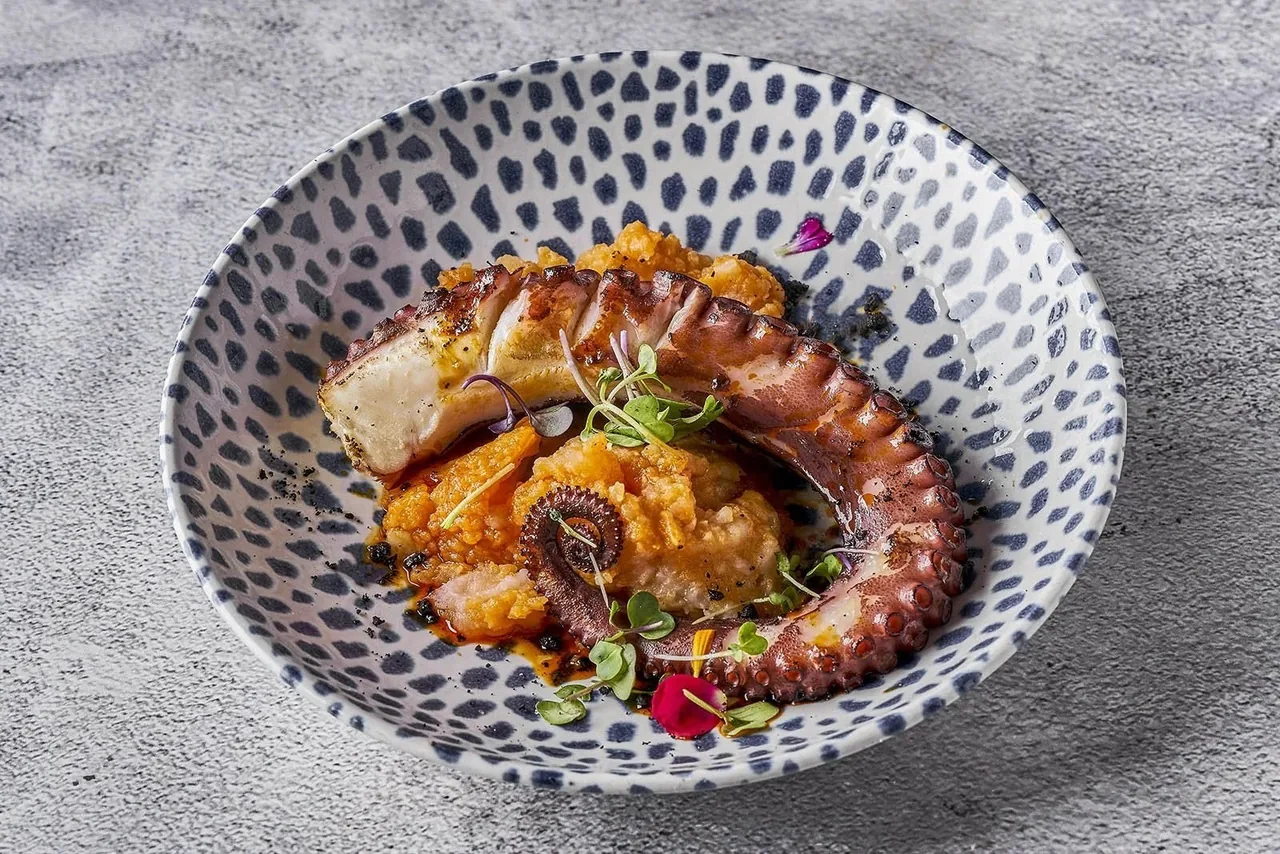 A patterned bowl of cooked octopus in orange sauce