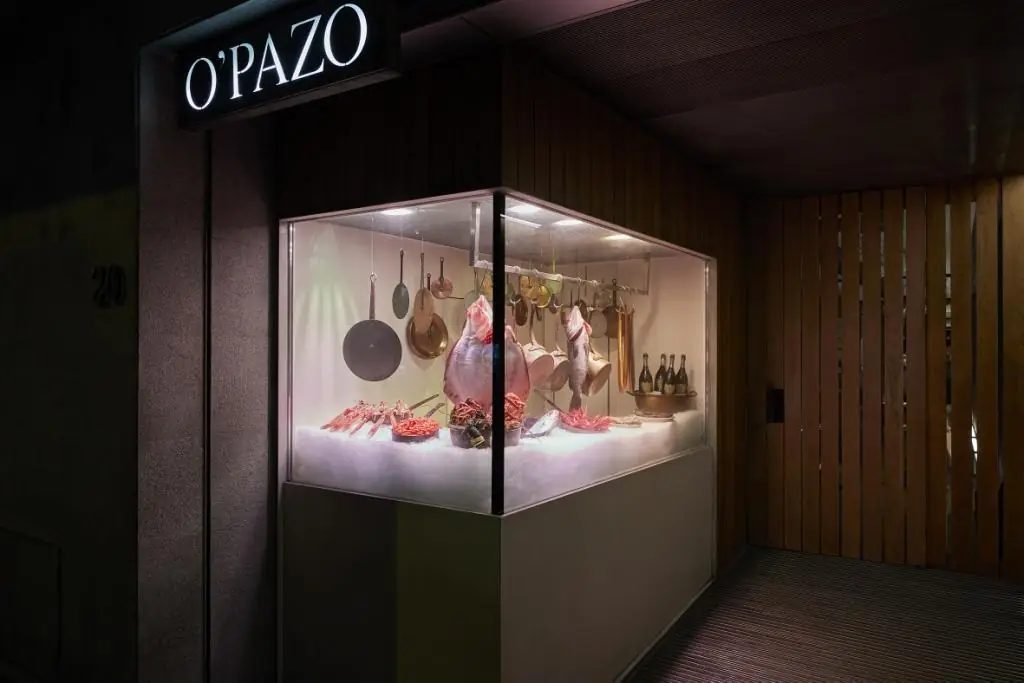 Lit glass display case at entrance with hanging ham, crab, fish and shellfish on ice