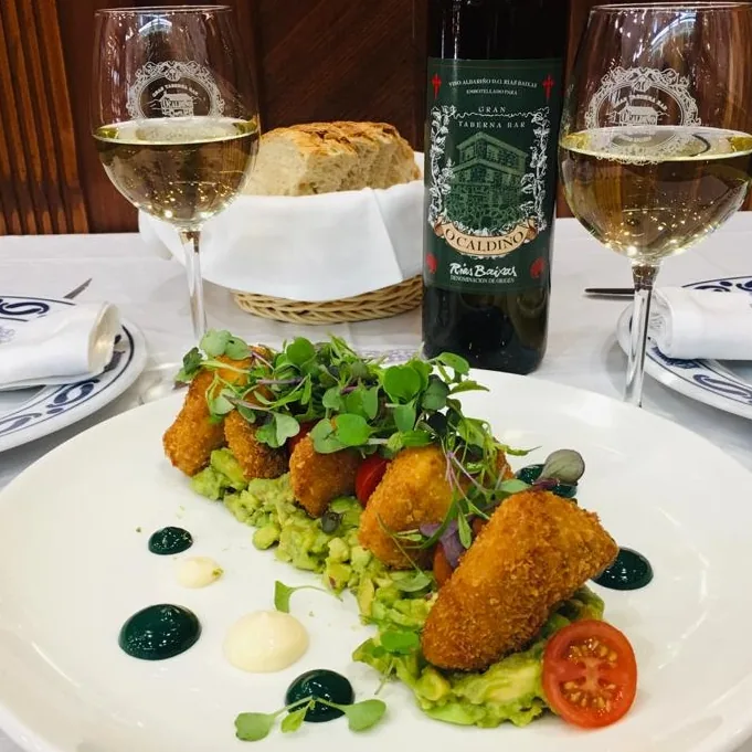 A plate of breaded croquettes beside two glasses of white wine