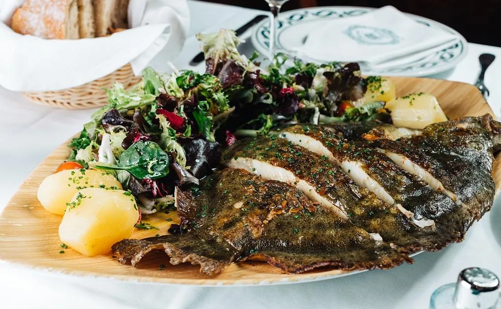 A grilled whole fish plated with mixed salad greens and potatoes