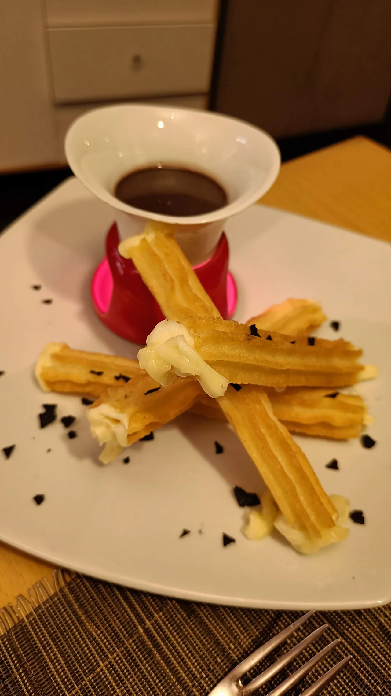 A plate of churros dusted with sugar next to a cup of chocolate dipping sauce