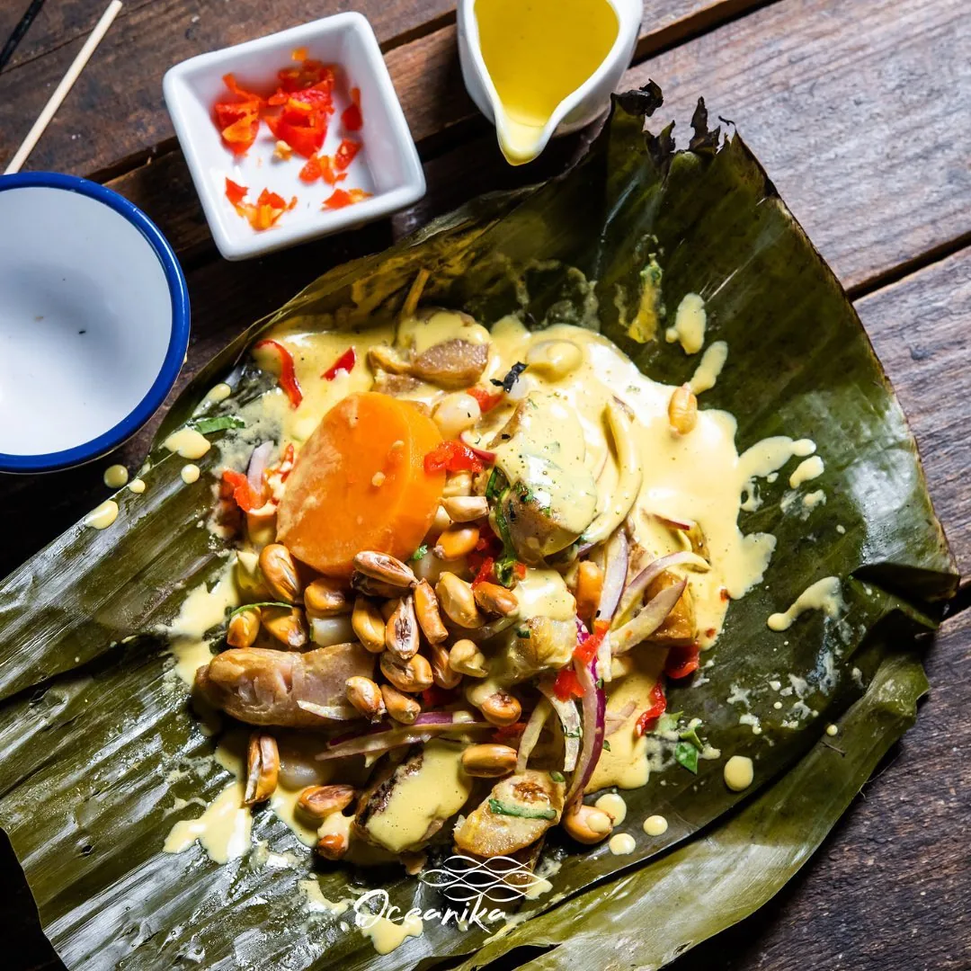 An overhead view of a seafood dish with mussels, corn and a fried egg on a banana leaf