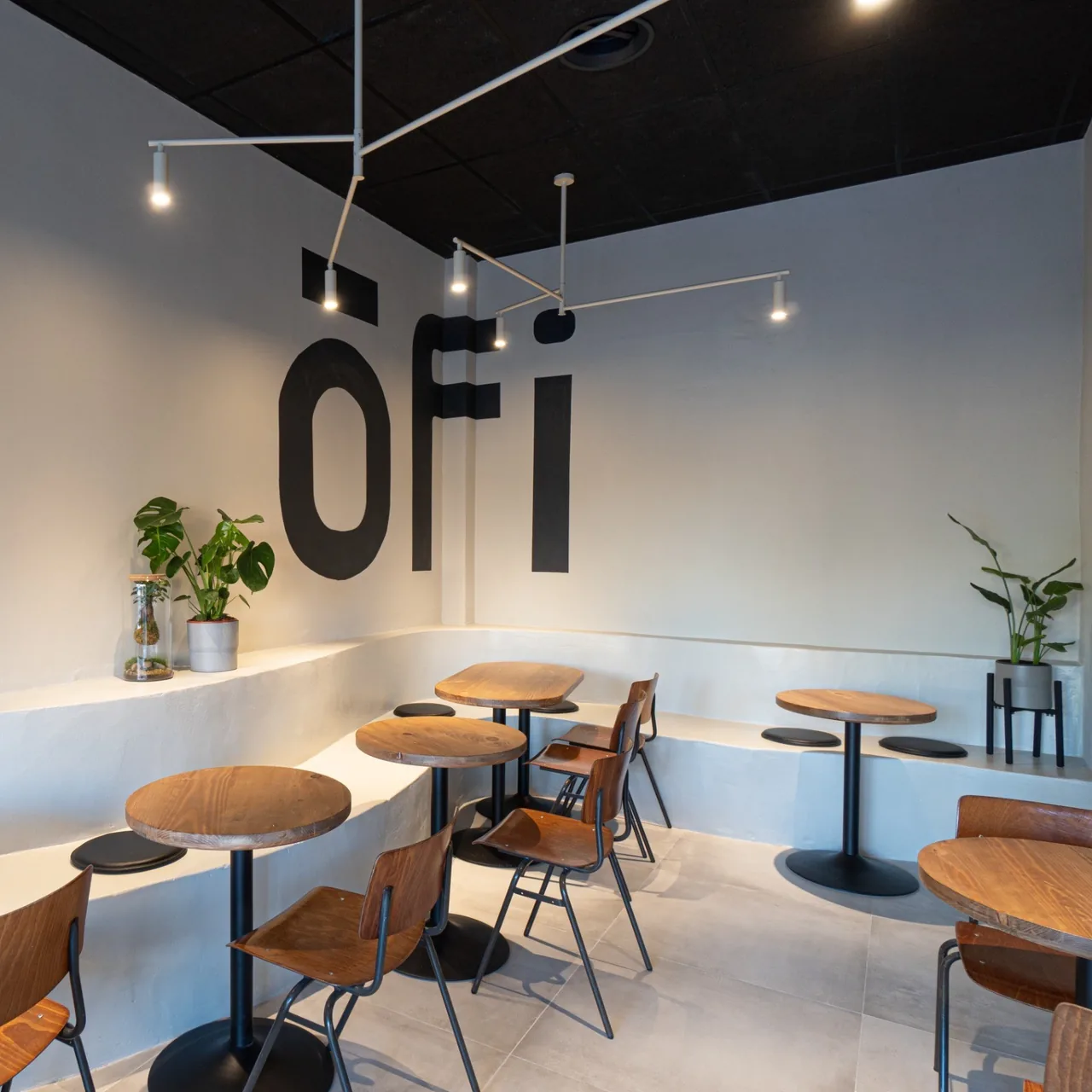 A bright cafe interior with round wooden tables, a white curved bench and a large logo on the wall