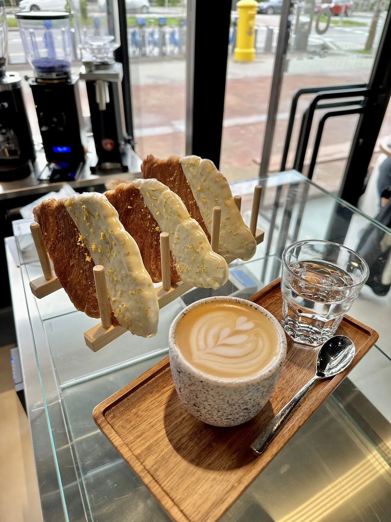 A latte with art on a wooden tray beside a stand of sliced pastries