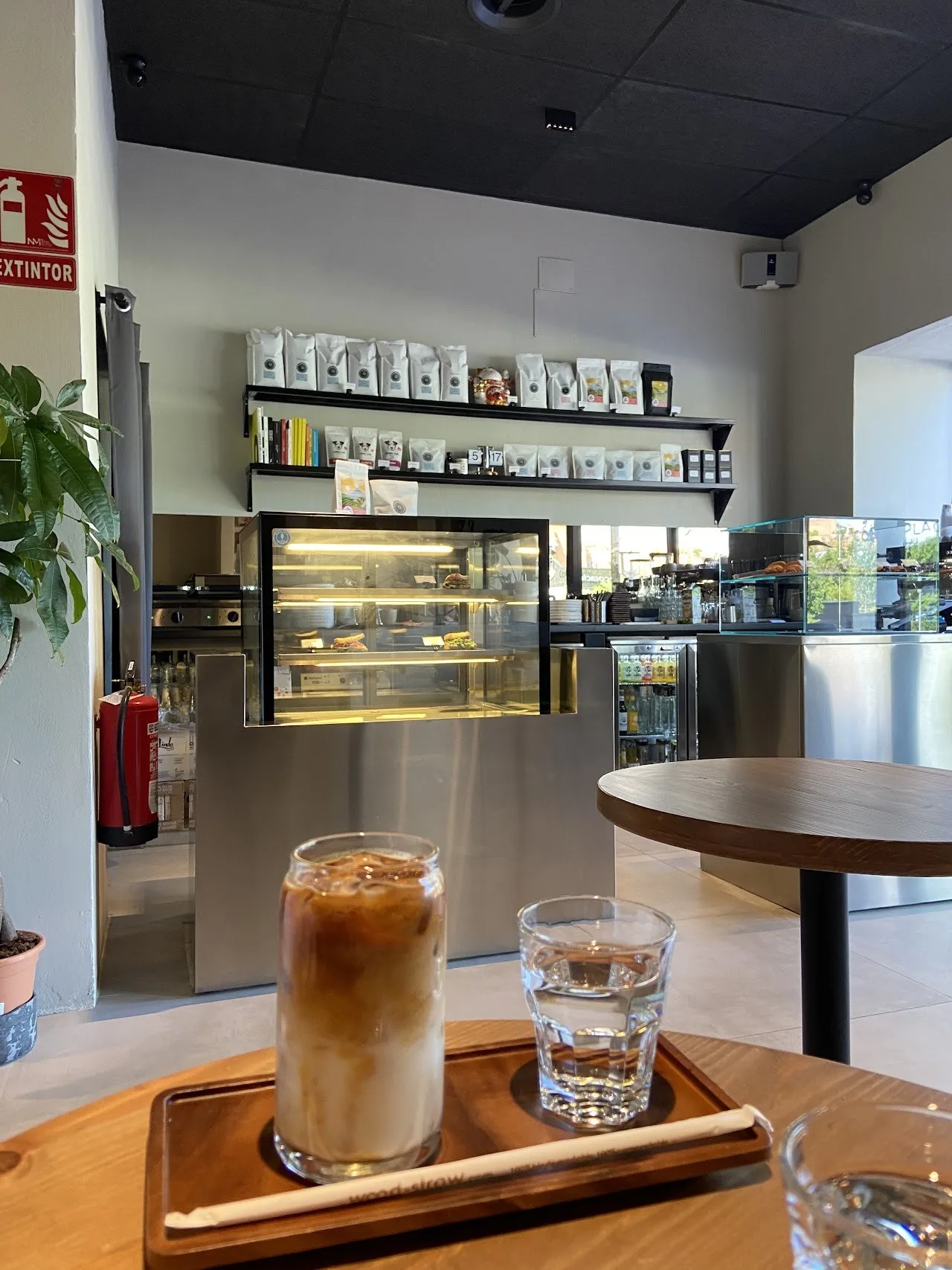 An iced coffee with milk in a glass on a small table with a cafe counter behind