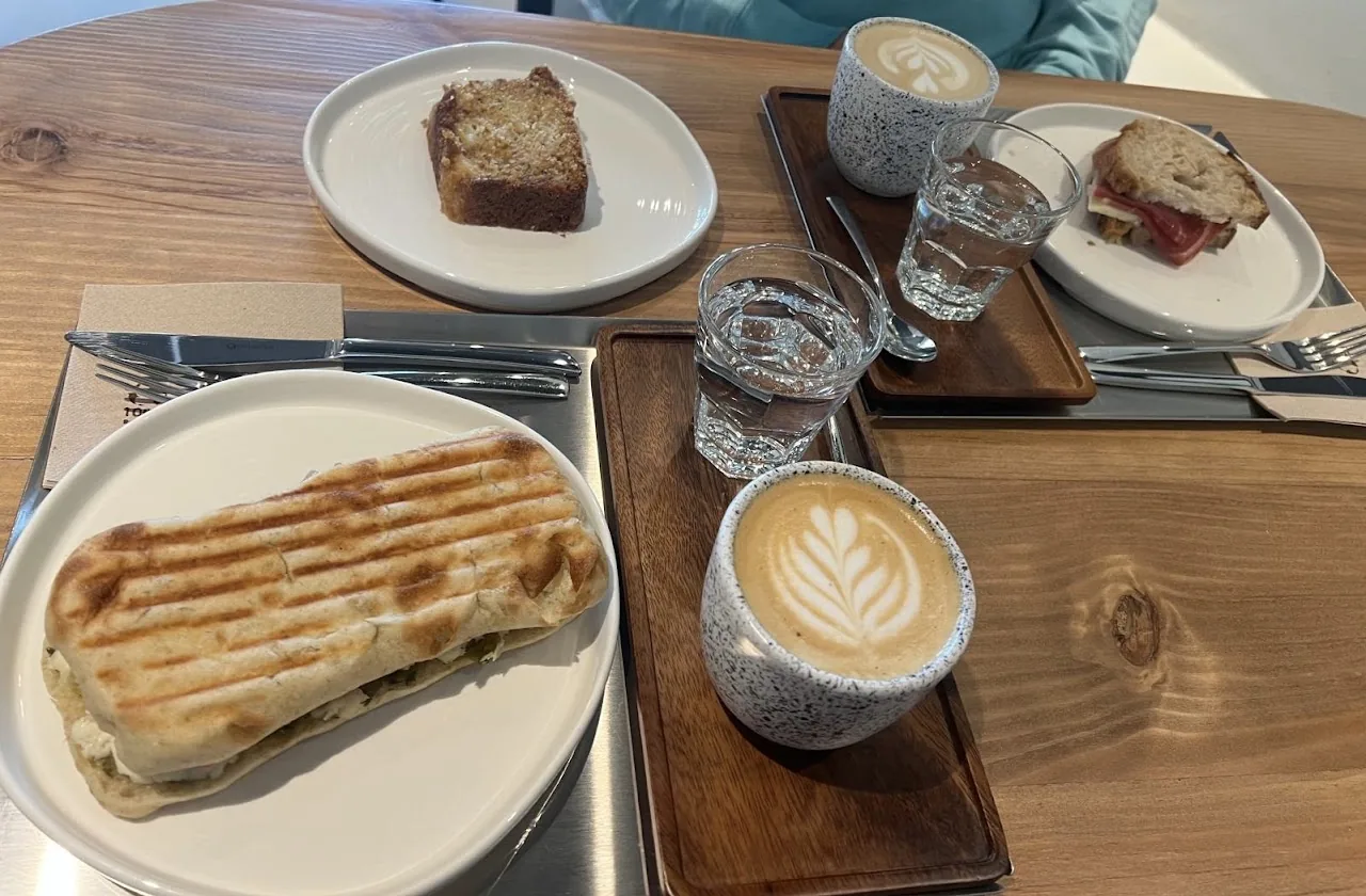 A slice of cake and a grilled panini sandwich beside two lattes