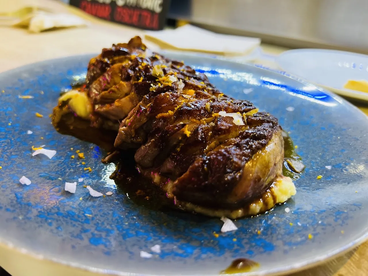 A blue plate with a glazed, wrapped meat dish garnished with sea salt flakes