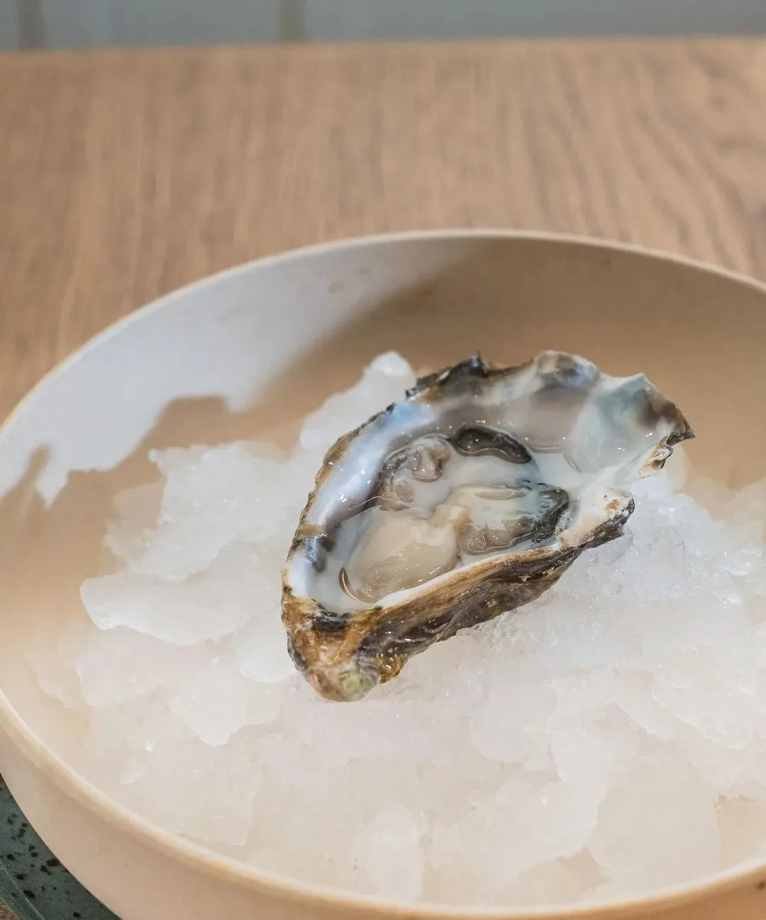 A single oyster on crushed ice in a white bowl