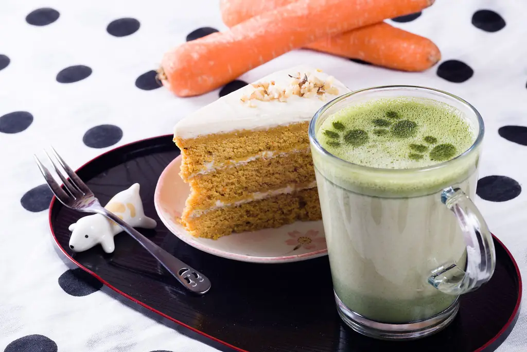 Carrot cake slice with walnuts beside a matcha latte on a tray