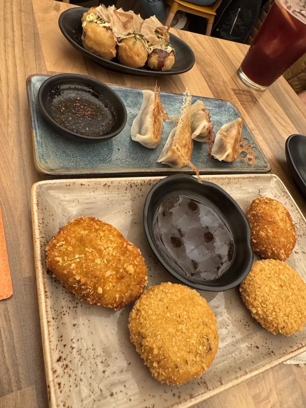 Takoyaki, crispy-skirted gyoza and breaded korokke on plates at the table