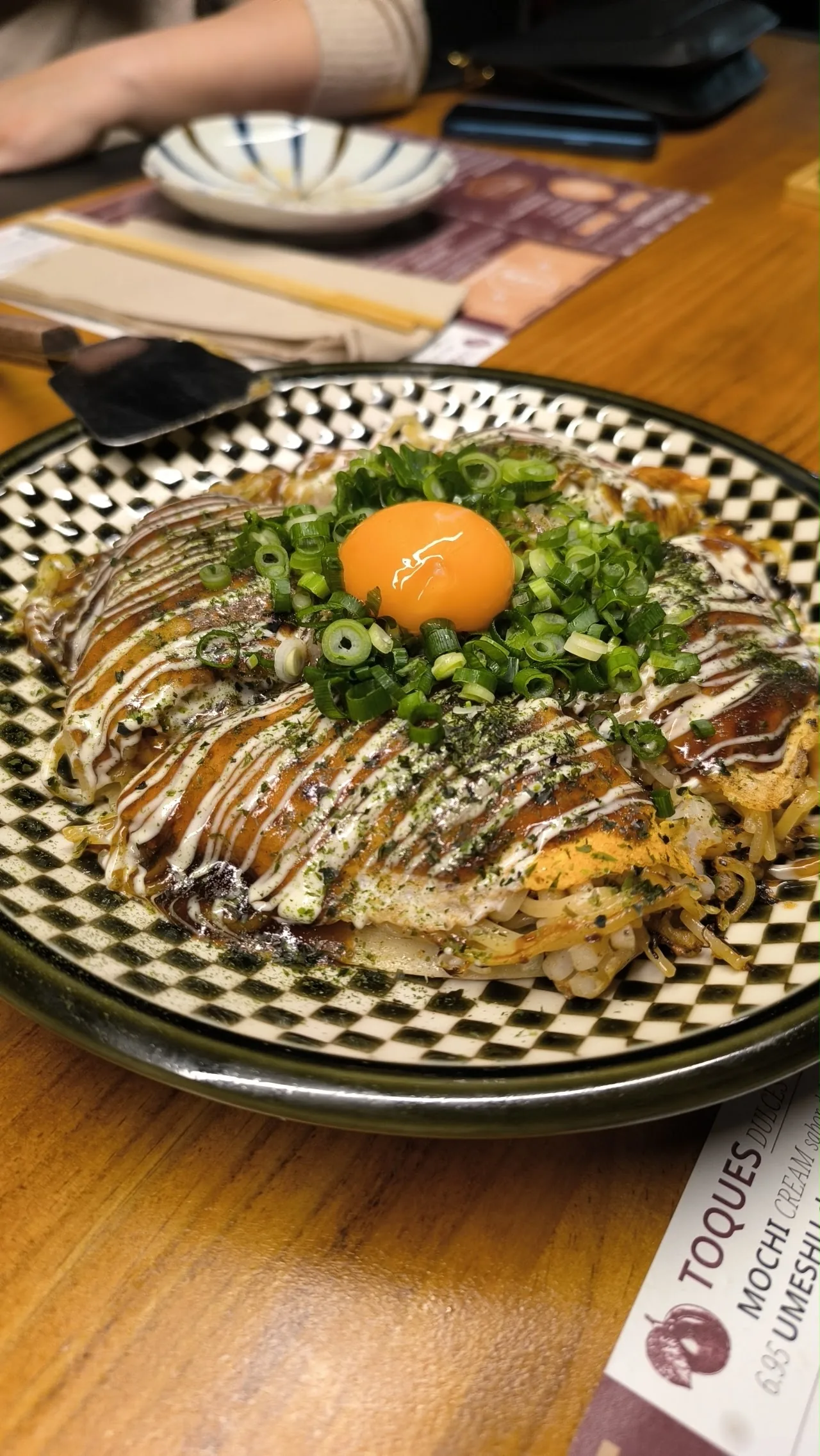 Okonomiyaki topped with a raw egg yolk and bonito flakes, drizzled with sauce